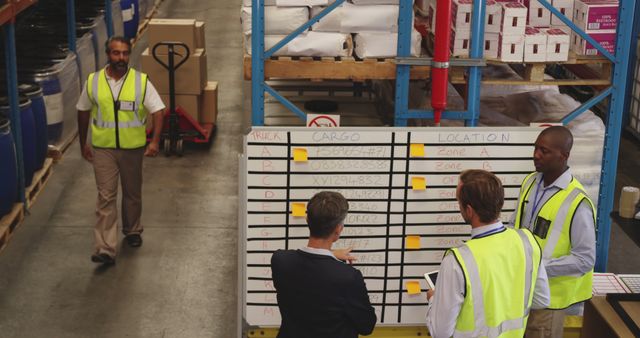 Team of workers gathering around whiteboard for planning and organizing logistics operations in warehouse. Effective for illustrating workplace teamwork, logistics management, and operational planning. Ideal for use in publications or materials related to supply chains, inventory management, and team coordination.