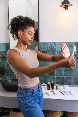 African american woman checking skin with handheld mirror at bathroom vanity for skincare