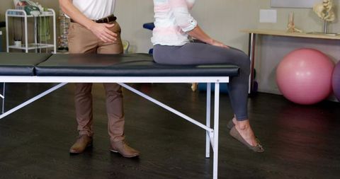 Physical therapist assessing seated woman on treatment table during spine rehab