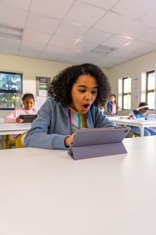 Elementary student reacting to tablet with surprised expression in bright classroom