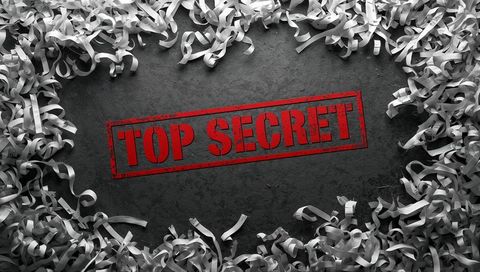 Top secret red stamp on dark textured surface surrounded by shredded paper