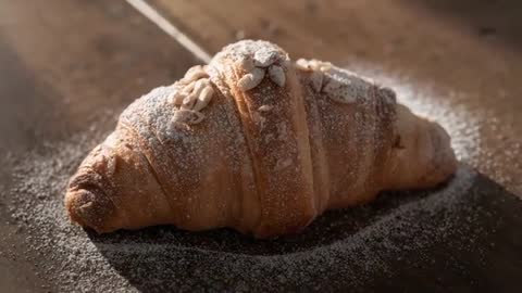 Pulling back revealing almond croissant dusted with powdered sugar on rustic dark board