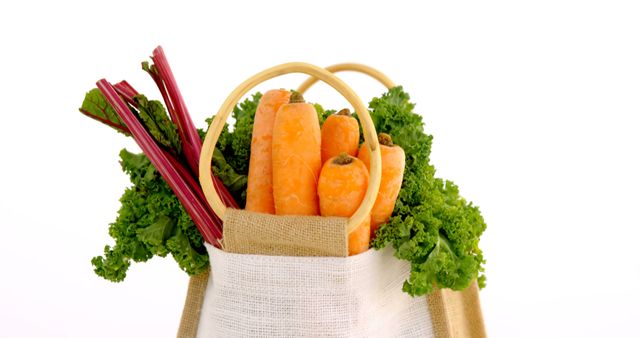 A reusable shopping bag is filled with fresh vegetables, including carrots and leafy greens, against a white background, with copy space. Highlighting the concept of healthy eating and sustainability, the image promotes the use of eco-friendly bags for grocery shopping.