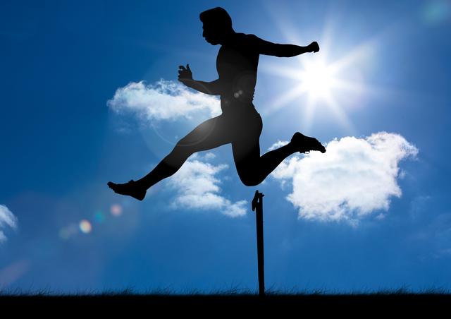 This dynamic image captures a silhouette of an athlete mid-jump over a hurdle, set against a clear blue sky with bright sunlight. Ideal for use in sports apparel advertisements, fitness promotion campaigns, motivational posters, and health-related articles. The image conveys themes of determination, strength, and athletic excellence.