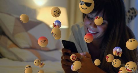 Woman interacting with emoticons using smartphone in bed