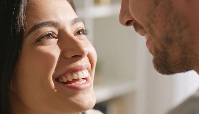 Smiling hispanic woman leaning toward partner sharing intimate laugh in sunlit living room