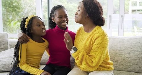 African American mother bonding with daughters on sofa smiling and chatting in living room
