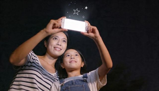 Mother and daughter holding smartphone looking up at glowing screen with star doodles