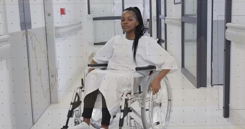 Sitting woman in wheelchair navigating hospital corridor showing mobility and resilience