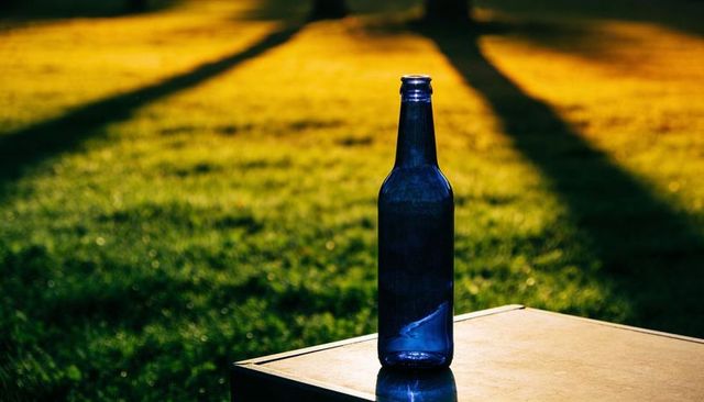 Cobalt Bottle Reflecting Sunlit Lawn and Long Tree Shadows on Outdoor Tabletop Evening Glow