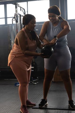 Two african american women partnering with kettlebell, working out in gym strength training