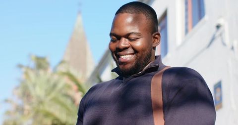 Smiling African American Man Wearing Zip Sweater and Crossbody Bag on Sunlit Urban Street