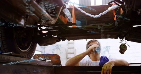 Mechanic drinking coffee in garage pit under vehicle during repair break
