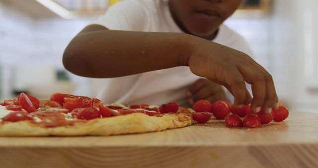 Happy african american boy adding tomatoes on pizza in kitchen - Download Free Stock Photos Pikwizard.com
