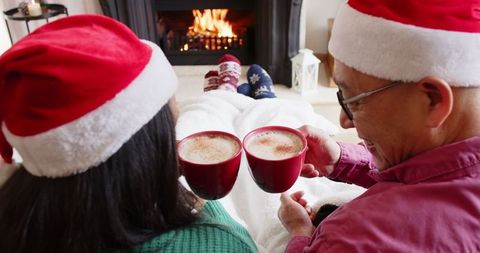 Senior couple toasting hot cocoa by fireplace in christmas spirit