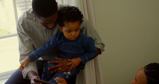 Front view of young black family using digital tablet in a comfortable home. Father holding baby boy on lap 4k