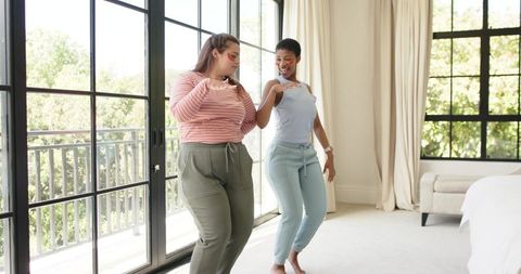 African american friends dancing in sunlit bedroom by glass balcony doors