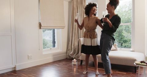African American women celebrating at home barefoot, laughing and toasting with champagne