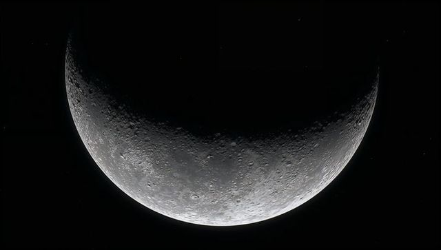 Crescent moon revealing detailed cratered surface along sharp terminator in space