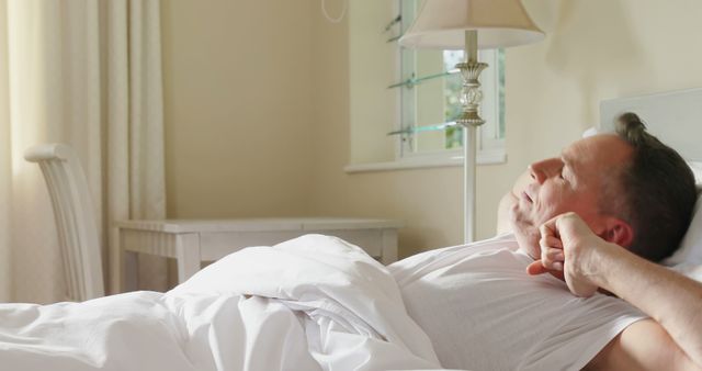 Middle-aged man stretching in bed after waking up in bright bedroom - Download Free Stock Images Pikwizard.com