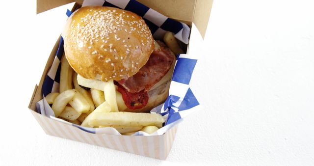 A gourmet burger with crispy fries in a takeaway box. The burger has a sesame bun and bacon, placed in a striped box over blue and white paper. Perfect for advertisements, food menus, fast food promotions, and food delivery services marketing.