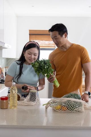 Asian couple unpacking groceries and inspecting fresh parsley on modern kitchen countertop