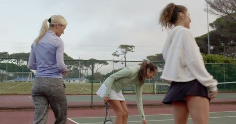 Three women practicing tennis on outdoor hardcourt in park during casual training session