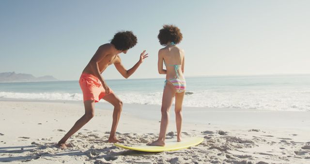 A brother and sister are practicing surfing techniques on a sand beach during a sunny day. Both are wearing swimsuits and seem to be having fun near the ocean waves. This can be used in summer vacation ads, beach activity promotions, or family bonding themes.