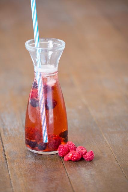 Bottle with berry cocktail and raspberry on wooden board