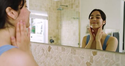 Woman Applying Skincare Routine in Elegant Bathroom Mirror Reflection