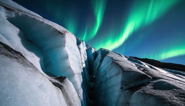 Northern lights illuminating deep glacial crevasse with ice seracs and moraine