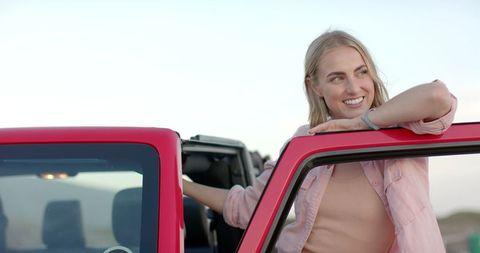 Cheerful young woman enjoying road trip adventure in red car