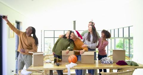 Multicultural friends taking festive selfie during holiday housewarming as unpacking boxes