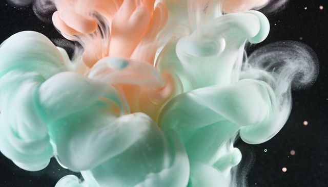 Swirling mint and peach ink plumes forming soft pastel clouds underwater macro fluid art