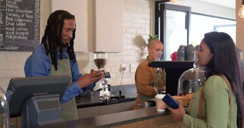 Indian woman ordering coffee from african american cashier as asian barista prepares espresso
