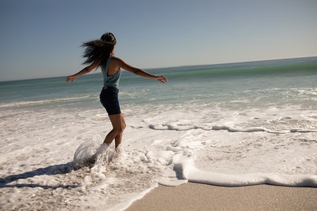 Biracial woman having fun on a beach, her arms outstretched, standing in water. Free time and vacation. 