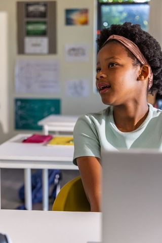 African American schoolgirl using laptop in bright classroom, engaged student learning