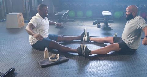 African american men stretching together on gym floor after workout, smiling and chatting