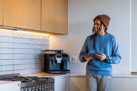 African american man using tablet in modern kitchen leaning on counter near espresso machine