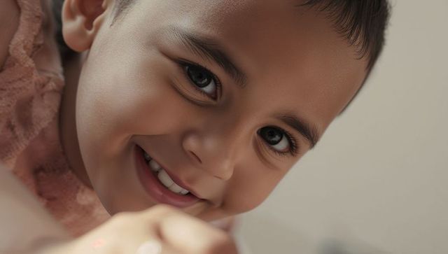 Smiling toddler boy leaning forward reaching out with bright eyes and playful grin in pink