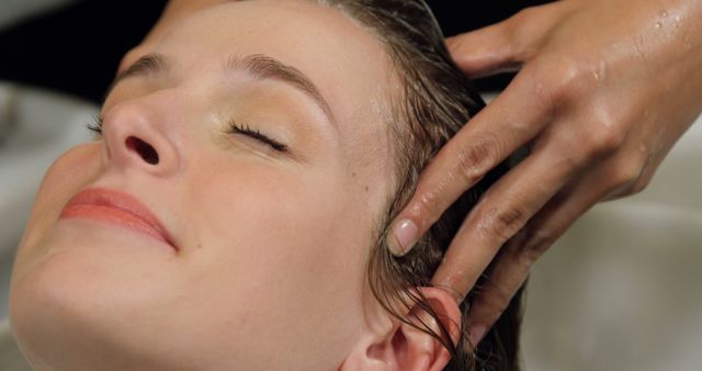 Woman relaxing while receiving a calming head massage at a hair salon. Ideal for use in promotions for hair salons, beauty spas, wellness centers, and advertising relaxation or head massage services. Suitable for websites, brochures, and social media posts focused on beauty and personal care.