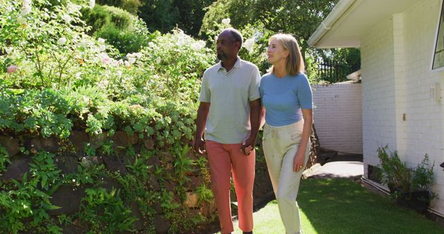 Diverse senior couple walking in their garden in the sun holding hands and talking. staying at home in isolation during quarantine lockdown.