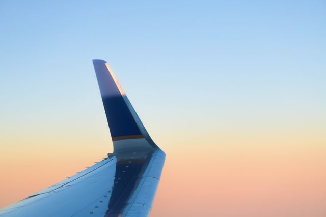 Airplane wing captured during golden hour, showing a serene sunset with clear sky. Ideal for travel blogs, airline promotions, vacation marketing, and articles related to aviation or air travel experiences.