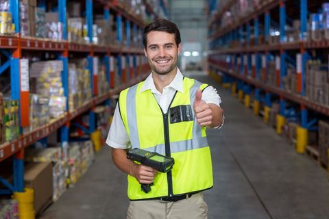 Confident warehouse worker giving thumbs up in distribution aisle