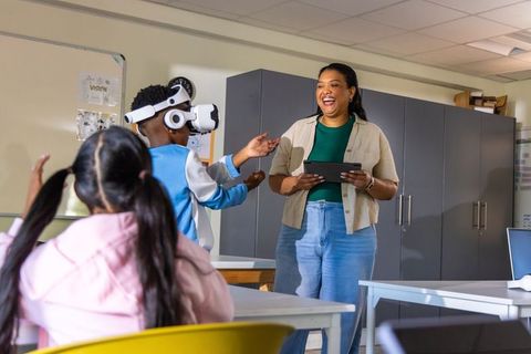 Teacher guiding students using vr headset in multicultural classroom, laughing and learning together