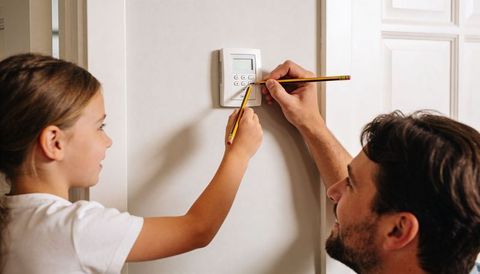 Father teaching daughter to program thermostat keypad in hallway, hands-on parenting moment