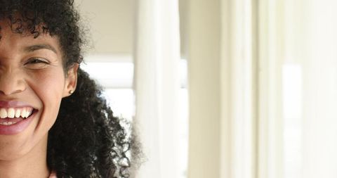 Headshot african american woman smiling by sunlit window with curly hair and natural light