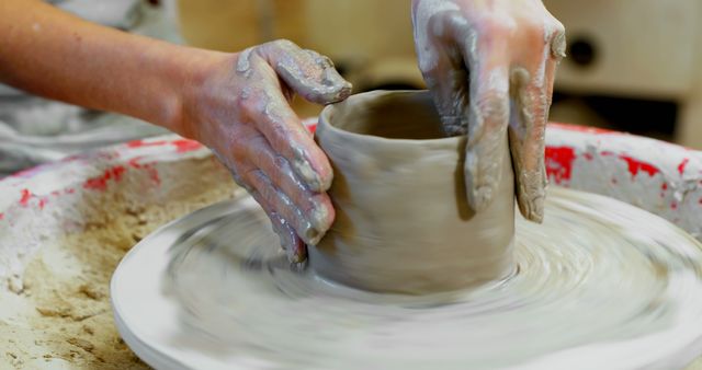 Hands shape a clay pot on a pottery wheel, capturing the essence of craftsmanship in ceramics. This process highlights the skill and creativity involved in the traditional art of pottery making.