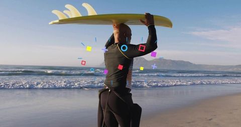 Mature surfer carrying yellow longboard overhead on sandy beach with rolling waves
