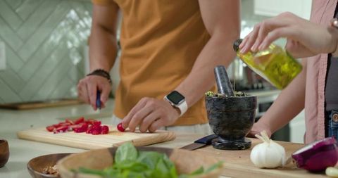 Couple cooking together chopping cherry tomatoes and pouring olive oil with mortar